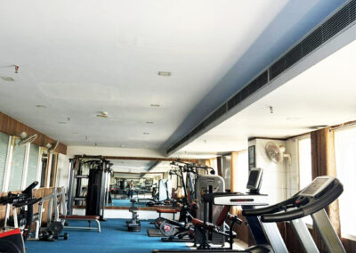 Modern gym interior with treadmills, dumbbells, weight machines, mirrors, and blue flooring in a spacious fitness center.